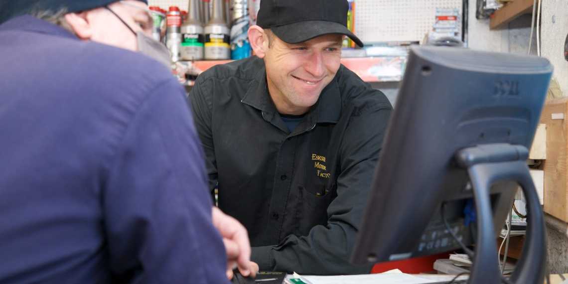 Male member of the Eskside team behind the trade counter looking at computer screen with a customer while smiling   